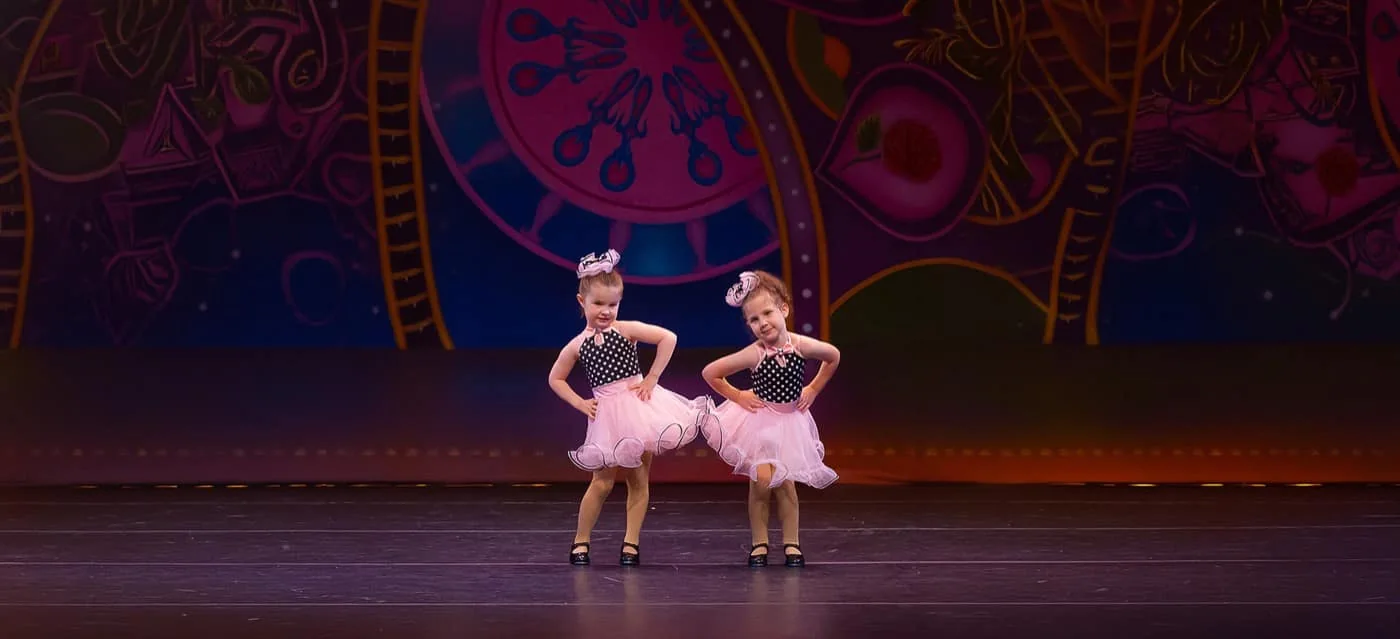 Two young Encore dancers in pink dresses performing on stage